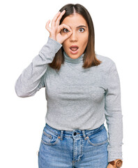 Young beautiful woman wearing casual turtleneck sweater doing ok gesture shocked with surprised face, eye looking through fingers. unbelieving expression.