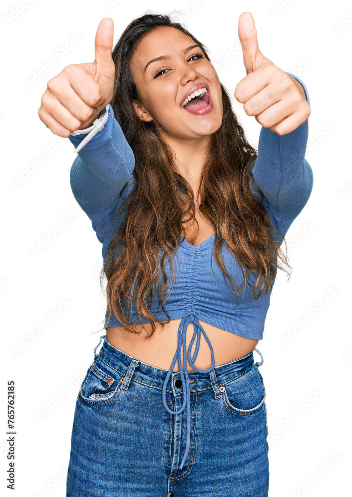 Wall mural Young hispanic girl wearing casual clothes approving doing positive gesture with hand, thumbs up smiling and happy for success. winner gesture.