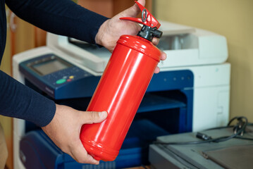 A man holds a fire extinguisher in his hands against the background of office equipment.