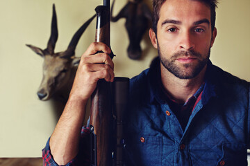 Hunting, trophy and portrait of man with gun for game shooting, adventure and hobby with confidence. Sports hunter and serious person in cabin with rifle, pride and animal head collection in home - obrazy, fototapety, plakaty