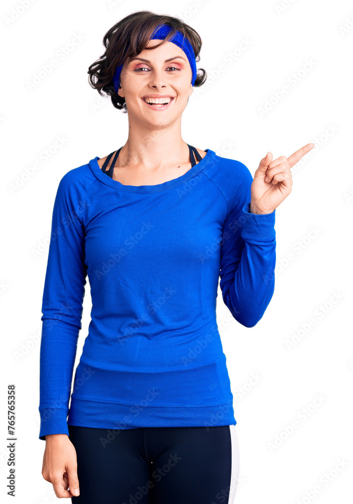 Wall mural beautiful young woman with short hair wearing training workout clothes with a big smile on face, poi