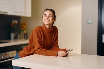 Happy young female enjoying leisure time at home, sitting on a white couch and smiling while...