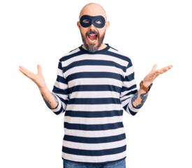 Young handsome man wearing burglar mask crazy and mad shouting and yelling with aggressive expression and arms raised. frustration concept.