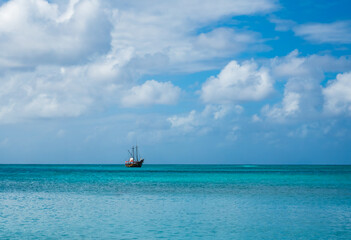 Pirate ship (tour boat) on the open turquoise water of the Caribbean Sea. Landscape photo of horizon and sky beautiful white clouds taken from Palm Beach, Noord, Aruba, Dutch island (February 2024).