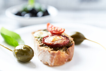 Crostini with tomato, salami and olive pesto on wooden background.	