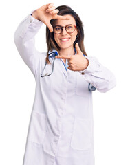Plakaty  Young beautiful woman wearing doctor stethoscope and glasses smiling making frame with hands and fingers with happy face. creativity and photography concept.