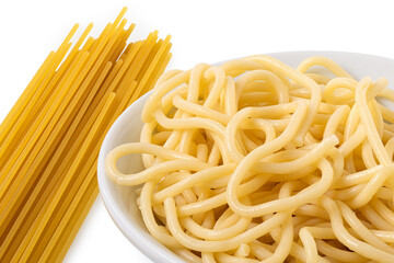 Detail of cooked spaghetti in a white ceramic bowl next to uncooked spaghetti on white.