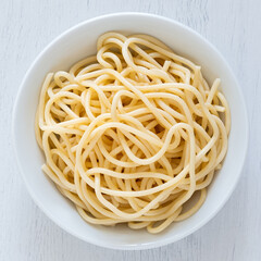 Cooked spaghetti in a white ceramic bowl isolated on white painted wood from above.