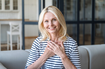 Portrait of happy mature woman holding hands on chest, feeling grateful