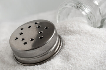 Glass salt shaker and metal lid lying on top of sea salt. - 765782534