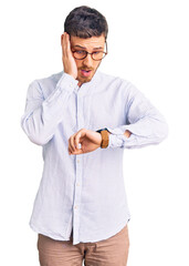 Handsome young man with bear wearing elegant business shirt and glasses looking at the watch time...