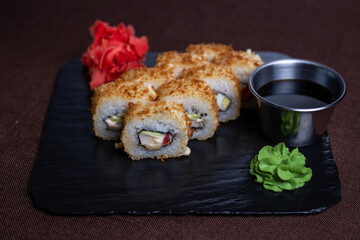 Deep-fried sushi roll with soy sauce and wasabi on a black stone plate