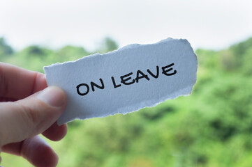 Hand holding torn paper with On Leave text with nature background. Annual leave concept