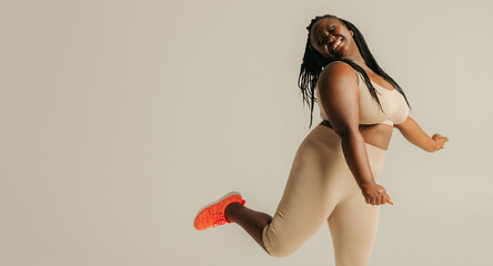 Full length happy plus size African woman in sportswear dancing on studio background