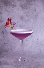 Elegant pink cocktail in a glass with flower garnish on a gray background