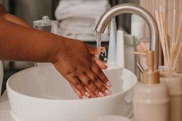 Close-up of plus size African woman covered in towel washing hands at the domestic bathroom - 765787198