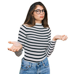 Young beautiful teen girl wearing casual clothes and glasses clueless and confused expression with...