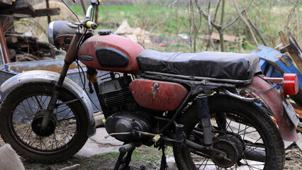 Old motorcycle in the dust. Red retro moto. Defective motorcycle, needs repair. A dirty rural gasoline motorcycle, next to it in the yard around the mess