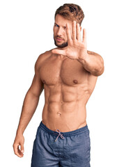 Young caucasian man standing shirtless doing stop sing with palm of the hand. warning expression...