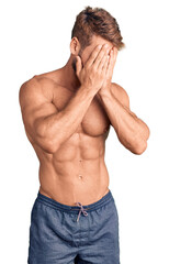 Young caucasian man standing shirtless with sad expression covering face with hands while crying....