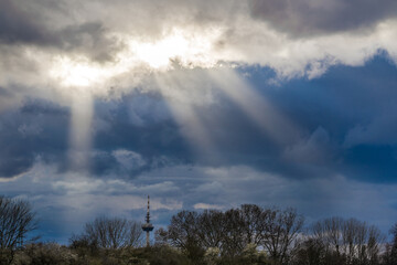 Sun rays in the dark blue sky over the trees and the TV tower, dramatic sky