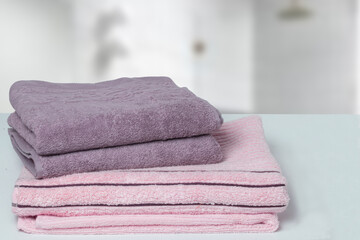 Obraz na płótnie Canvas Table top on towels background. Closeup of a stack or pile of violet and pink soft terry bath towels at a bright table against blurred bathroom background. Space.