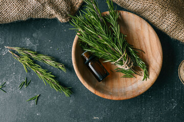 A bottle of essential oil with fresh rosemary twigs on a dark background