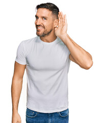 Fototapeta premium Handsome man with beard wearing casual white t shirt smiling with hand over ear listening an hearing to rumor or gossip. deafness concept.
