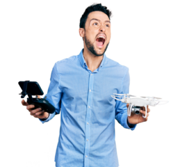 Hispanic man with beard using drone with remote control angry and mad screaming frustrated and furious, shouting with anger looking up.