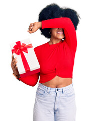 Young african american girl holding gift smiling cheerful playing peek a boo with hands showing...