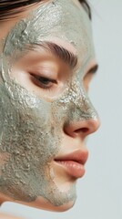 Fototapeta premium Close-up of a young beautiful woman with a green detox face mask, highlighting her serene gaze and the texture of the skincare product on her flawless skin.
