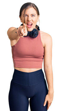 Beautiful caucasian young woman wearing gym clothes and using headphones pointing displeased and frustrated to the camera, angry and furious with you