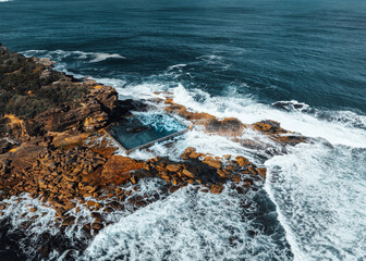 Aerial view early morning light with ocean waves flowing over rocks around North Curl Curl ocean rock pool during storm.
