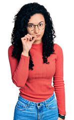 Young hispanic woman with curly hair wearing glasses mouth and lips shut as zip with fingers....