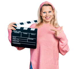 Young caucasian woman holding video film clapboard smiling happy pointing with hand and finger