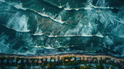 Fototapeten Top-down shot of a coastal town with houses lined up near the foamy waves and sandy beach. © Jonas