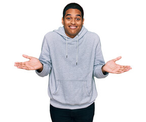 Young handsome hispanic man wearing casual sweatshirt clueless and confused expression with arms...
