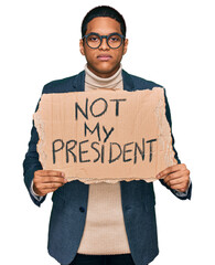 Young handsome hispanic man holding not my president protest banner thinking attitude and sober...