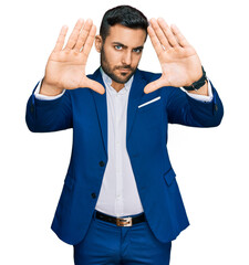 Young hispanic man wearing business jacket doing frame using hands palms and fingers, camera perspective