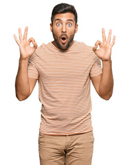Fototapeta premium Handsome hispanic man wearing casual clothes looking surprised and shocked doing ok approval symbol with fingers. crazy expression