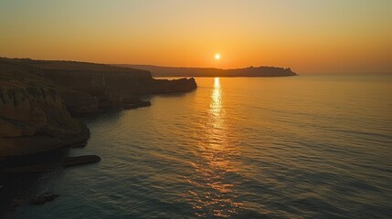Fototapeta premium A tranquil sunset over a calm sea with cliffs on one side.
