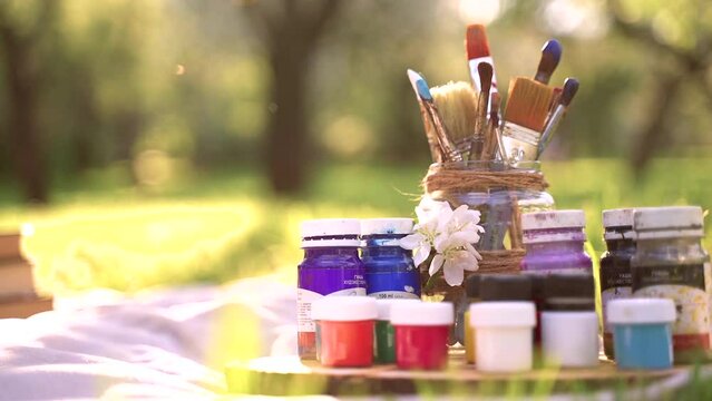 Paints and brushes in a glass jar in nature.Brushes in paint.Paints and brushes in the garden. Jars of paints. Wooden frame with paints. Plein air
