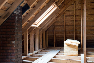 Wood-beamed attic with window. House construction. Roof insulation.