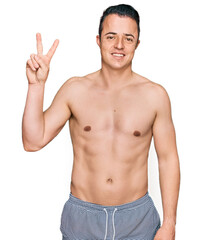 Fototapeta premium Handsome young man wearing swimwear shirtless showing and pointing up with fingers number two while smiling confident and happy.