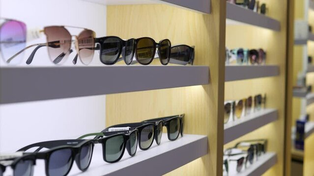 Boutique shelf wide range stylish sunglasses. Shelf with models in various shapes, colors designs from leading brands. Buyer can study all options and choose perfect pair of glasses placed shelf.