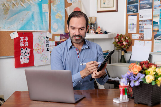 Experimentado profesor adulto latino dando clases de japon&eacute;s en l&iacute;nea en su estudio casero. Explicando con la tableta, formato para redes sociales