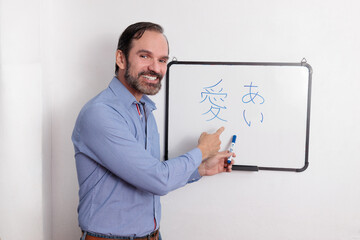 Profesor adulto latino dando clases de japonés en pequeña pizarra acrílica. Dando énfasis en lo...