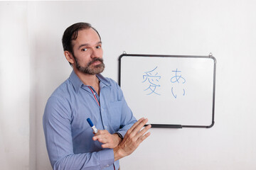 Profesor adulto latino dando clases de japonés en pequeña pizarra acrílica. Indicando...