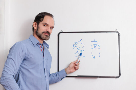 Profesor adulto latino dando clases de japonés en pequeña pizarra acrílica. Mirando seriamente a los alumnos