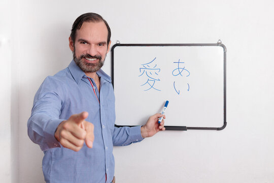 Profesor adulto latino dando clases de japonés en pequeña pizarra acrílica. Señalando a los estudiantes